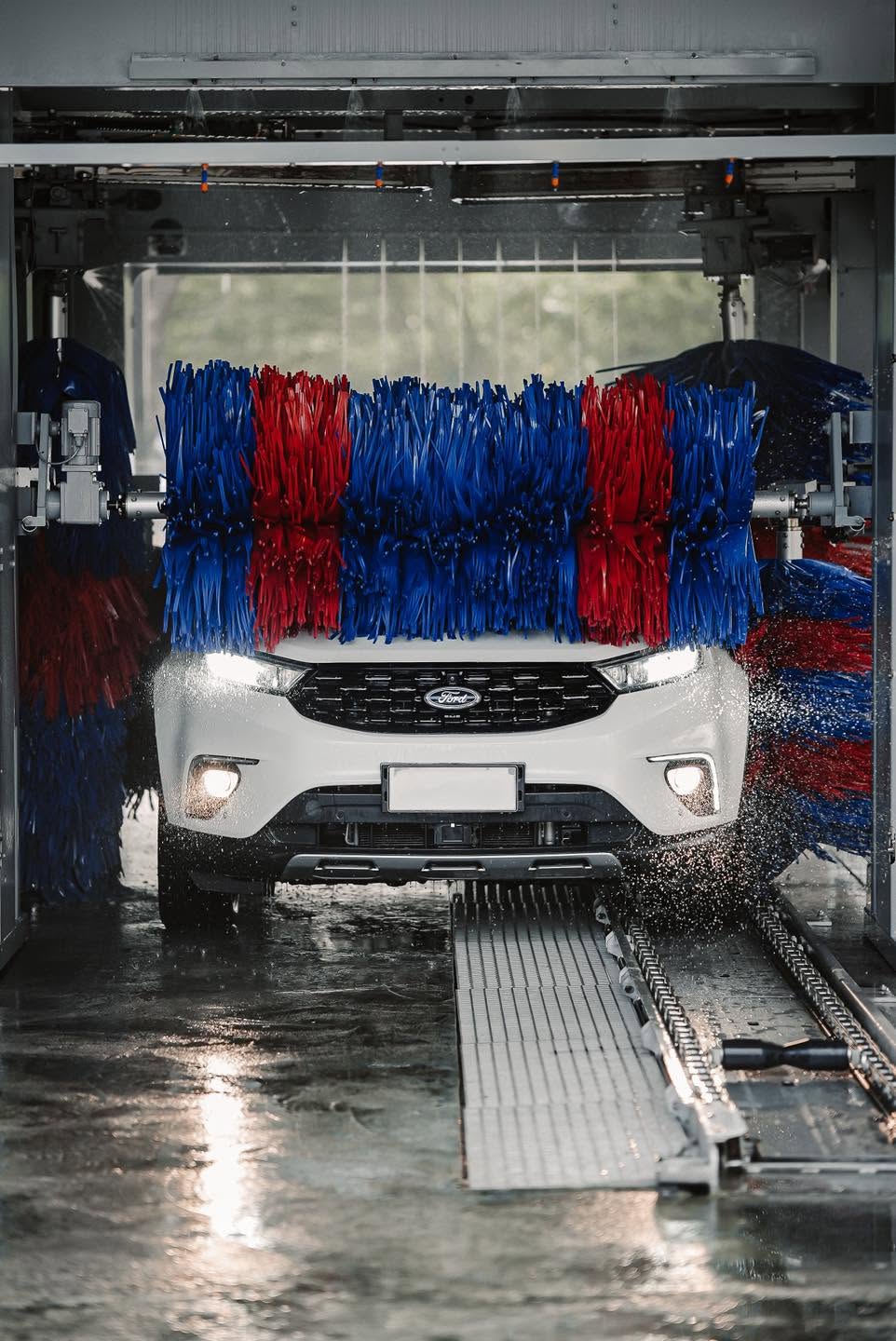 A white SUV moving through the CASPA Xtreme automatic car wash with blue and red brushes and water spray
